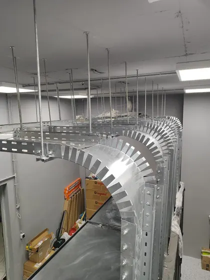 Overhead galvanised cable tray turning a wide radius corner through a finished office ceiling void, suspended on threaded rod