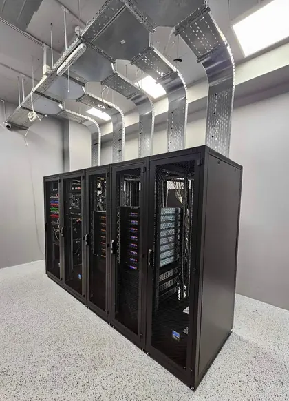 A completed row of five black server cabinets in a data centre room, each fed from above by its own galvanised tray drop