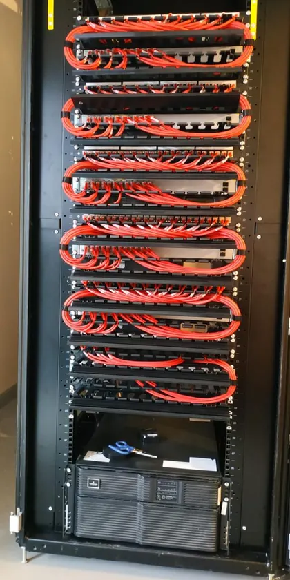Red patch leads looped in even horizontal service bows between patch panels and switches through a full rack, with a UPS at the base
